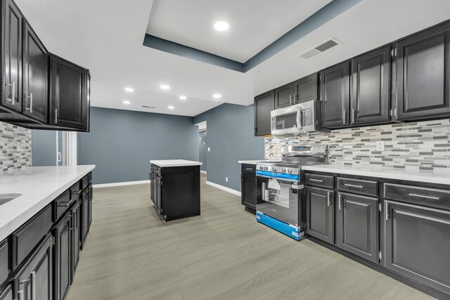 kitchen featuring light stone countertops, stainless steel appliances, a raised ceiling, tasteful backsplash, and light wood-type flooring