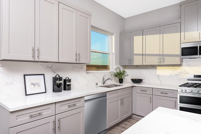 kitchen with backsplash, gray cabinets, sink, and appliances with stainless steel finishes