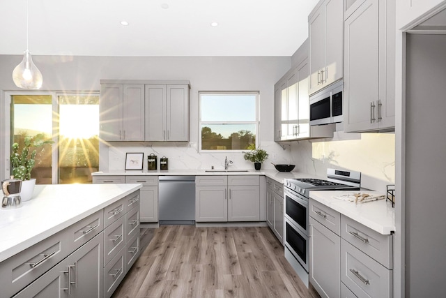 kitchen featuring sink, gray cabinets, light wood-type flooring, decorative light fixtures, and stainless steel appliances