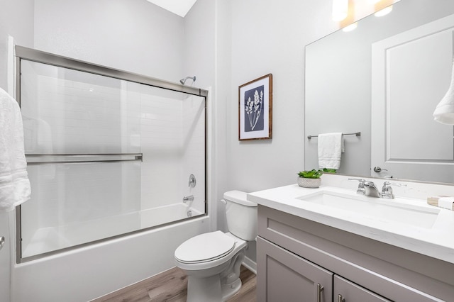 full bathroom with hardwood / wood-style flooring, vanity, toilet, and bath / shower combo with glass door