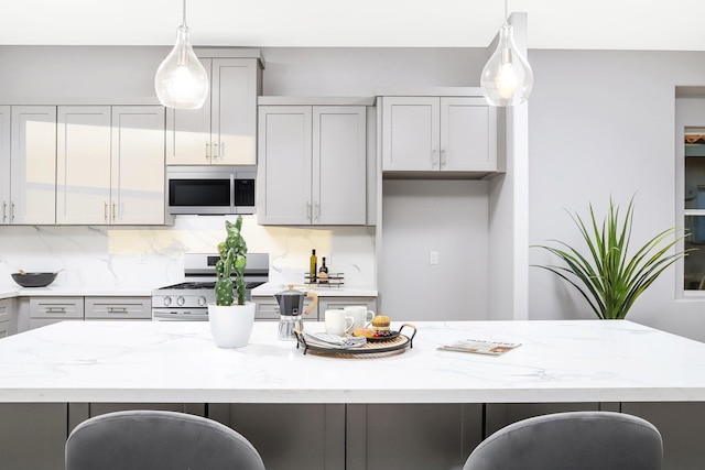 kitchen with a center island, gray cabinets, light stone countertops, and stainless steel appliances