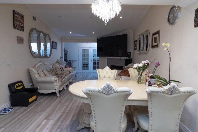 dining area with a fireplace, light hardwood / wood-style floors, crown molding, and an inviting chandelier