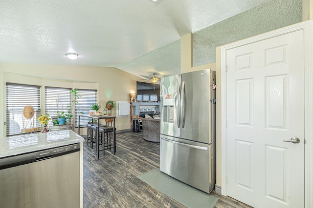 kitchen with dark wood-type flooring, stainless steel appliances, ceiling fan, vaulted ceiling, and a tile fireplace