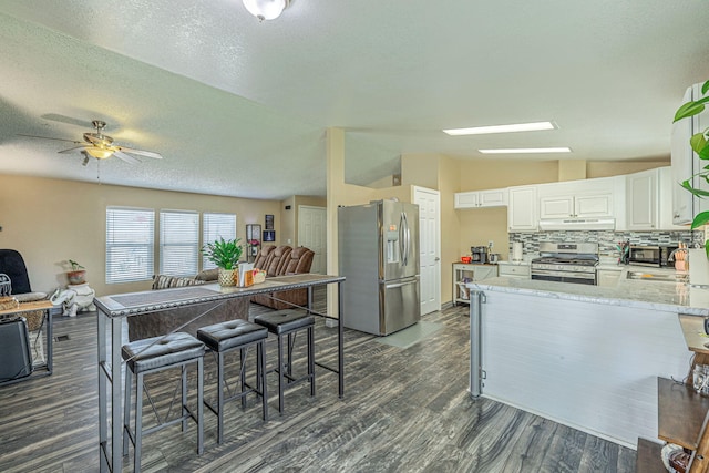 kitchen featuring open floor plan, white cabinets, stainless steel appliances, and vaulted ceiling