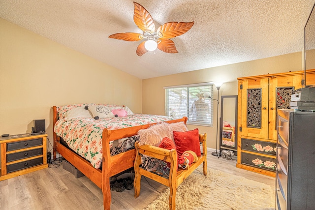 bedroom with ceiling fan, a textured ceiling, light wood-style flooring, and vaulted ceiling