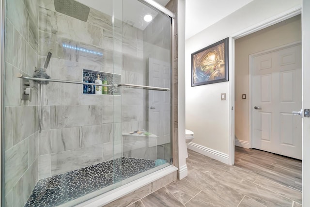 bathroom featuring toilet, a shower stall, and baseboards