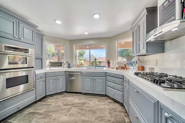 kitchen featuring recessed lighting, gray cabinets, light countertops, appliances with stainless steel finishes, and wall chimney range hood