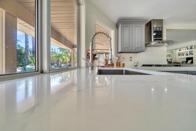 kitchen featuring extractor fan, gray cabinetry, a sink, light stone countertops, and stovetop