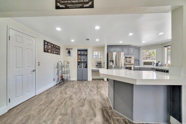 kitchen featuring recessed lighting, gray cabinetry, stainless steel appliances, a peninsula, and light countertops