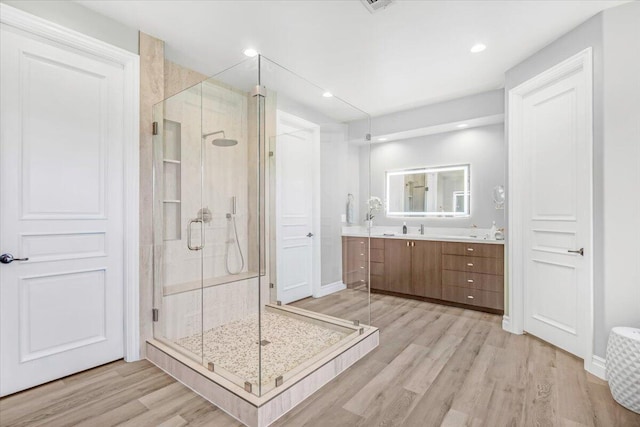 full bath with double vanity, a sink, a shower stall, and wood finished floors