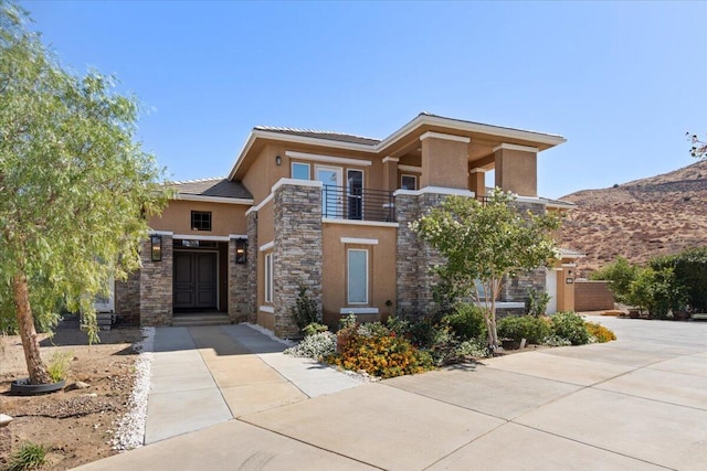 prairie-style house featuring stone siding, a mountain view, a balcony, and stucco siding