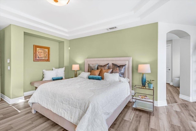 bedroom featuring baseboards, visible vents, a tray ceiling, and wood finished floors