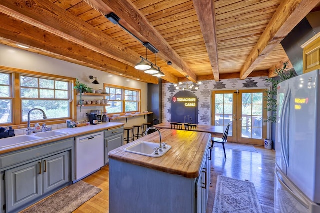 kitchen featuring white dishwasher, a kitchen island with sink, decorative light fixtures, beamed ceiling, and stainless steel refrigerator