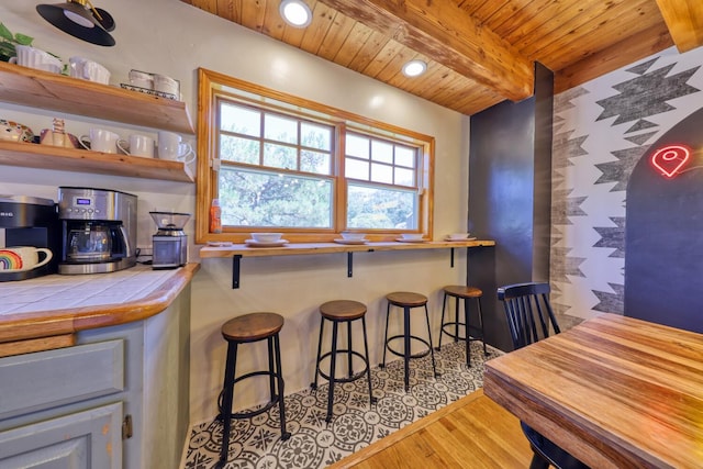 bar featuring beamed ceiling, tile counters, light wood-type flooring, and wood ceiling