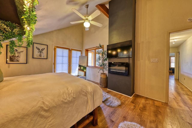 bedroom with a large fireplace, ceiling fan, beam ceiling, hardwood / wood-style flooring, and high vaulted ceiling