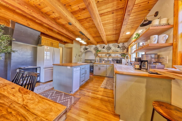 kitchen featuring white refrigerator, light hardwood / wood-style floors, beam ceiling, tile counters, and a kitchen island