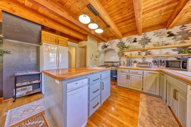 kitchen featuring hanging light fixtures, beamed ceiling, light hardwood / wood-style floors, white appliances, and a center island with sink