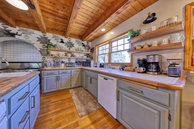 kitchen featuring light wood-type flooring, wood ceiling, beam ceiling, dishwasher, and tile counters