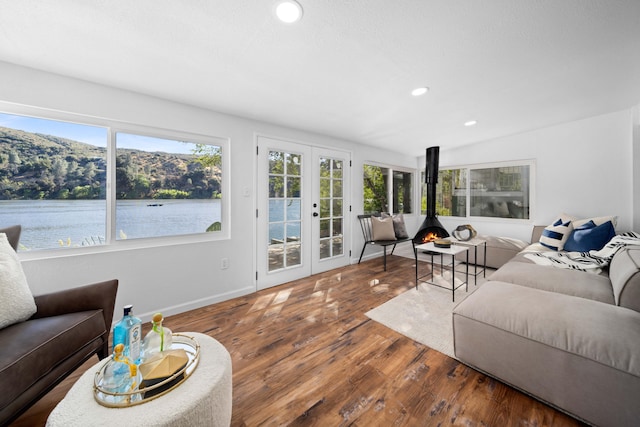 living room with wood finished floors, a water view, a wood stove, french doors, and recessed lighting