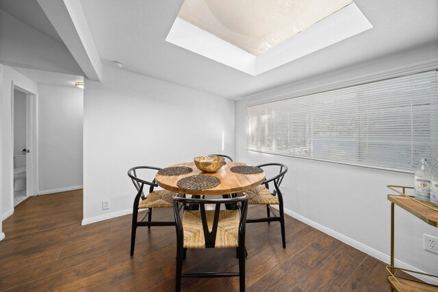 dining space with a skylight, baseboards, and dark wood finished floors