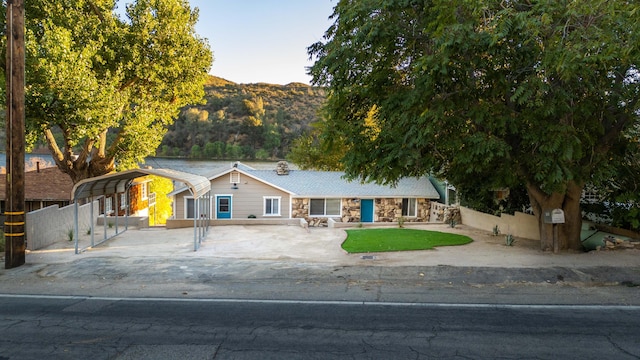 view of front of property featuring stone siding, a carport, fence, and a mountain view