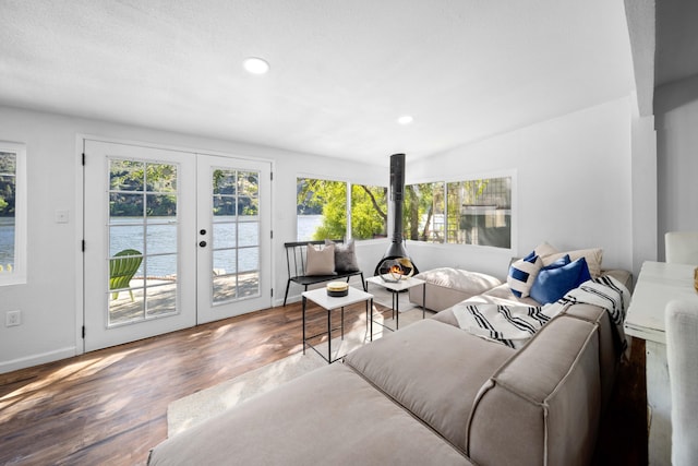 living room featuring wood finished floors, a water view, a wood stove, french doors, and recessed lighting
