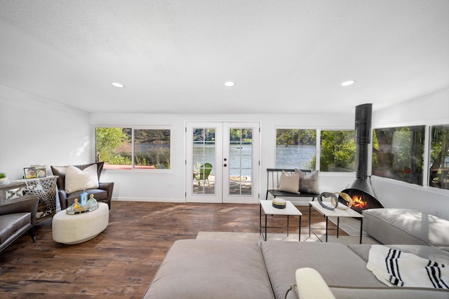 living area with dark wood-style floors, french doors, recessed lighting, a water view, and a wood stove