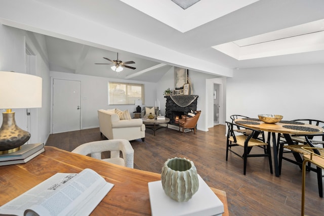 dining area with a lit fireplace, vaulted ceiling with skylight, dark wood-type flooring, and a ceiling fan