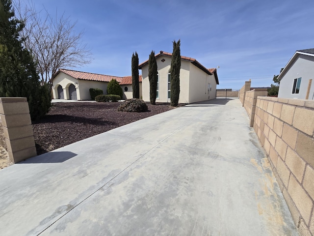 view of property exterior with fence, stucco siding, driveway, and a tile roof