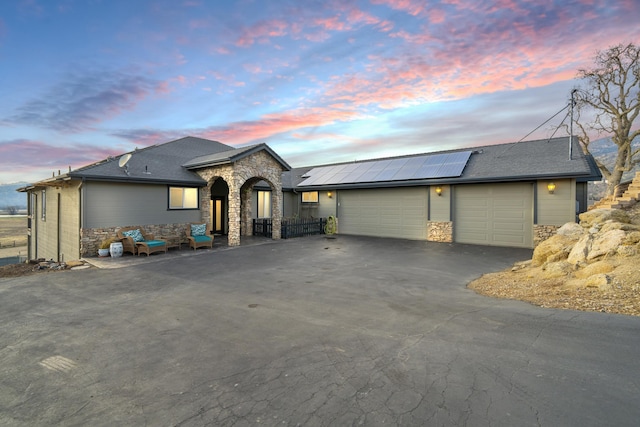 view of front of home with stone siding, driveway, roof mounted solar panels, and an attached garage