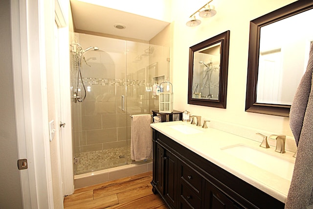 bathroom featuring double vanity, wood finished floors, a stall shower, and a sink