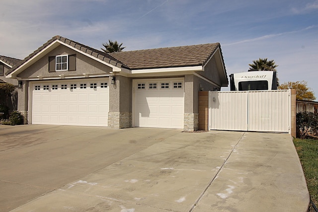 view of front of property featuring stucco siding, a garage, stone siding, driveway, and a gate