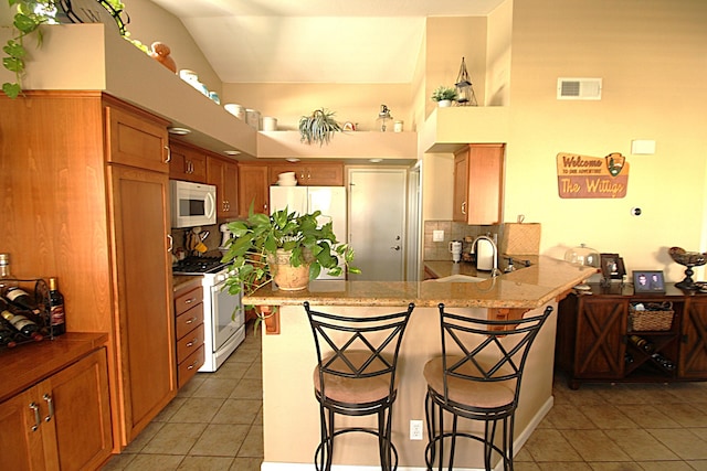 kitchen featuring white appliances, a peninsula, light tile patterned flooring, a sink, and a kitchen breakfast bar