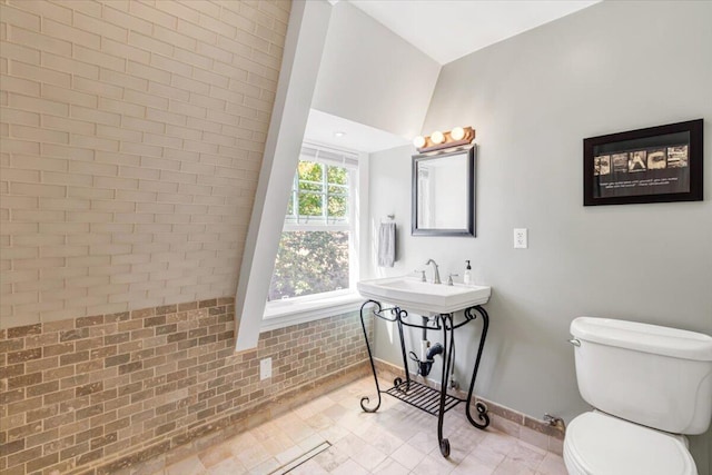 bathroom featuring sink, brick wall, lofted ceiling, and toilet