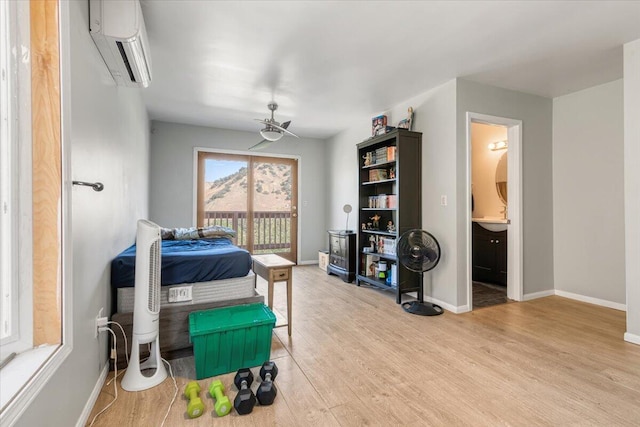 bedroom featuring ceiling fan, a wall mounted AC, ensuite bathroom, access to outside, and light wood-type flooring