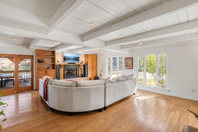 living room featuring beamed ceiling, a large fireplace, built in features, and light hardwood / wood-style flooring