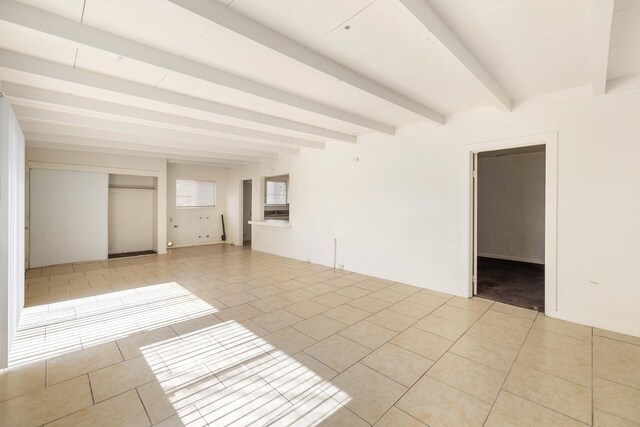 empty room with beam ceiling and light tile patterned floors