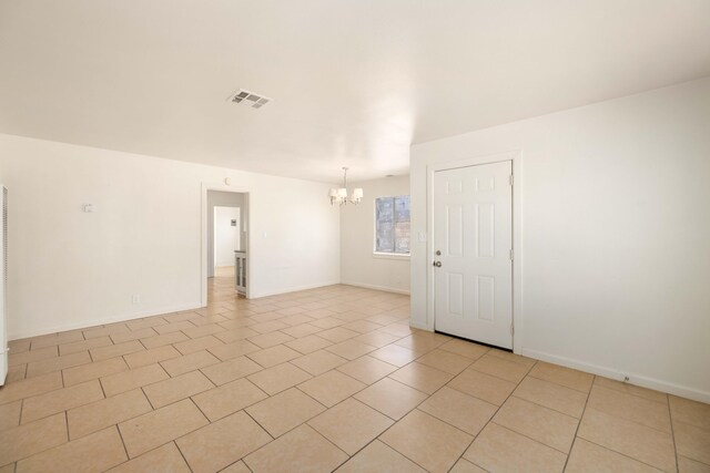 tiled spare room with a notable chandelier