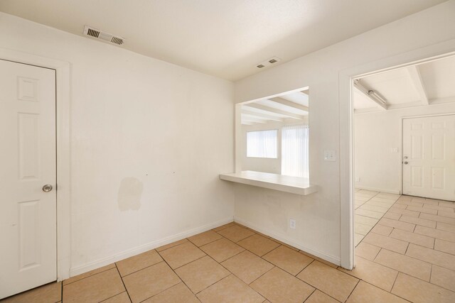 empty room featuring beamed ceiling and light tile patterned floors