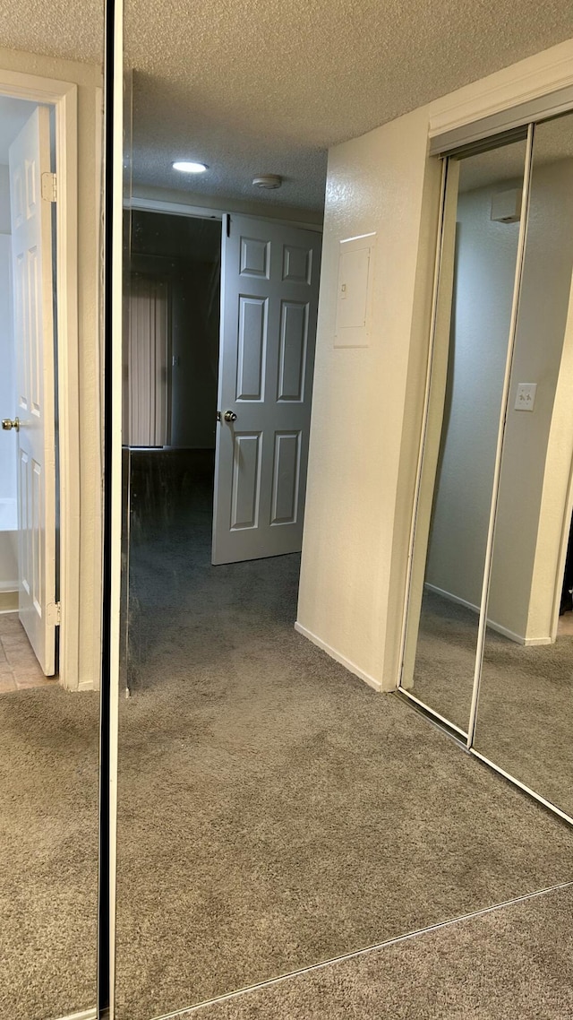 hallway featuring carpet, baseboards, and a textured ceiling