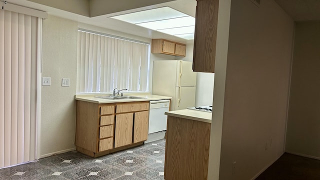 kitchen with a textured wall, white appliances, light countertops, and a sink