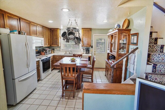 kitchen with light tile patterned floors, white appliances, a textured ceiling, and sink