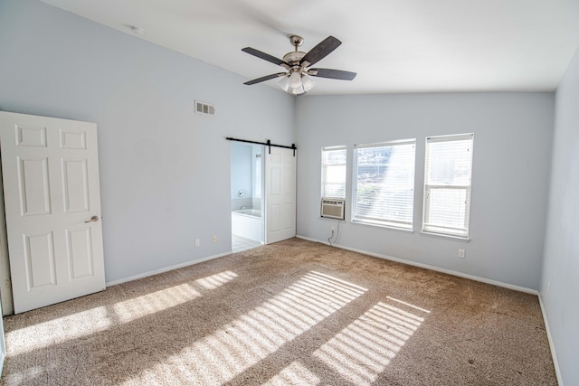 unfurnished bedroom featuring connected bathroom, ceiling fan, a barn door, vaulted ceiling, and carpet