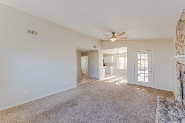 unfurnished living room featuring ceiling fan with notable chandelier, a stone fireplace, lofted ceiling, and light carpet