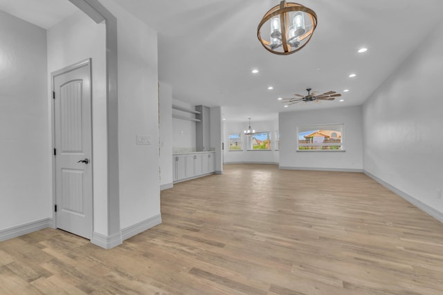 unfurnished living room featuring ceiling fan with notable chandelier and light hardwood / wood-style floors