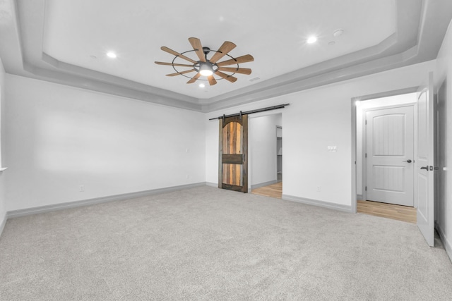 interior space featuring a tray ceiling, a barn door, ceiling fan, and light colored carpet