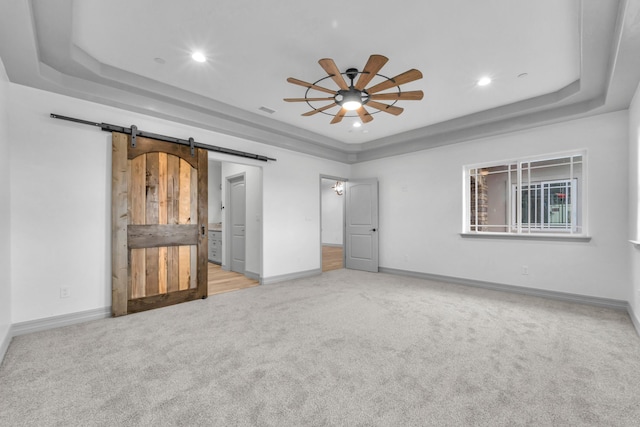 unfurnished bedroom with ceiling fan, a barn door, a raised ceiling, and light carpet