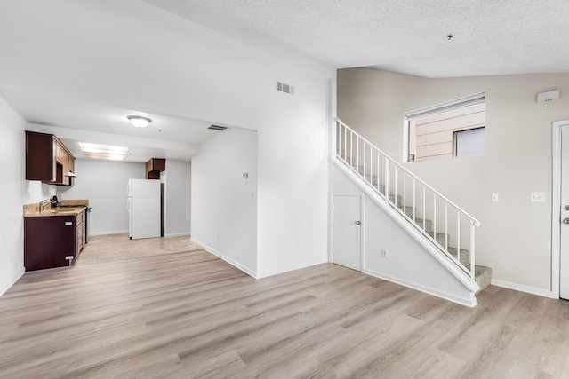 unfurnished living room featuring light hardwood / wood-style floors, sink, and a textured ceiling