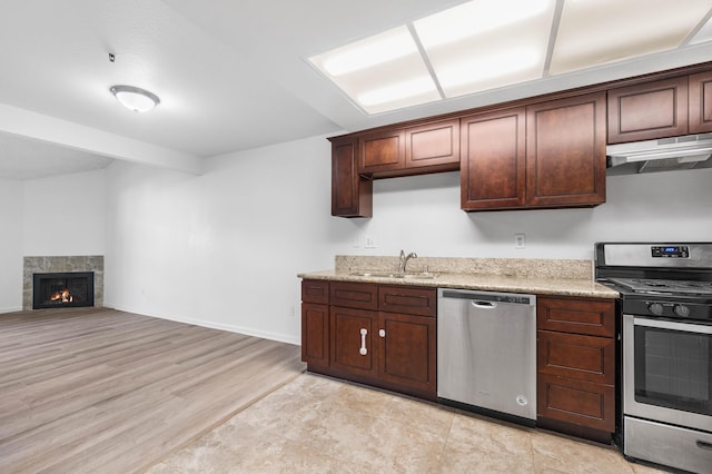 kitchen featuring a fireplace, appliances with stainless steel finishes, light stone countertops, and sink