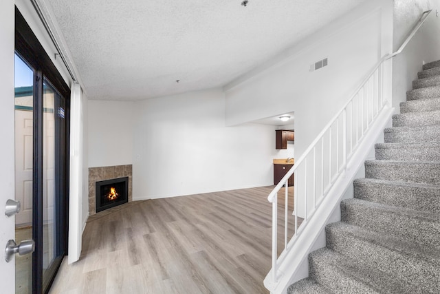 unfurnished living room featuring a tile fireplace, a textured ceiling, and light wood-type flooring